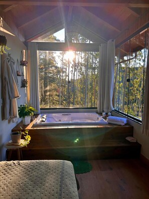 A room with a wooden bench, a bathtub, and a large window with a view of trees. - Chalé Sossego da Montanha RanchoQueimado (Rancho Queimado)