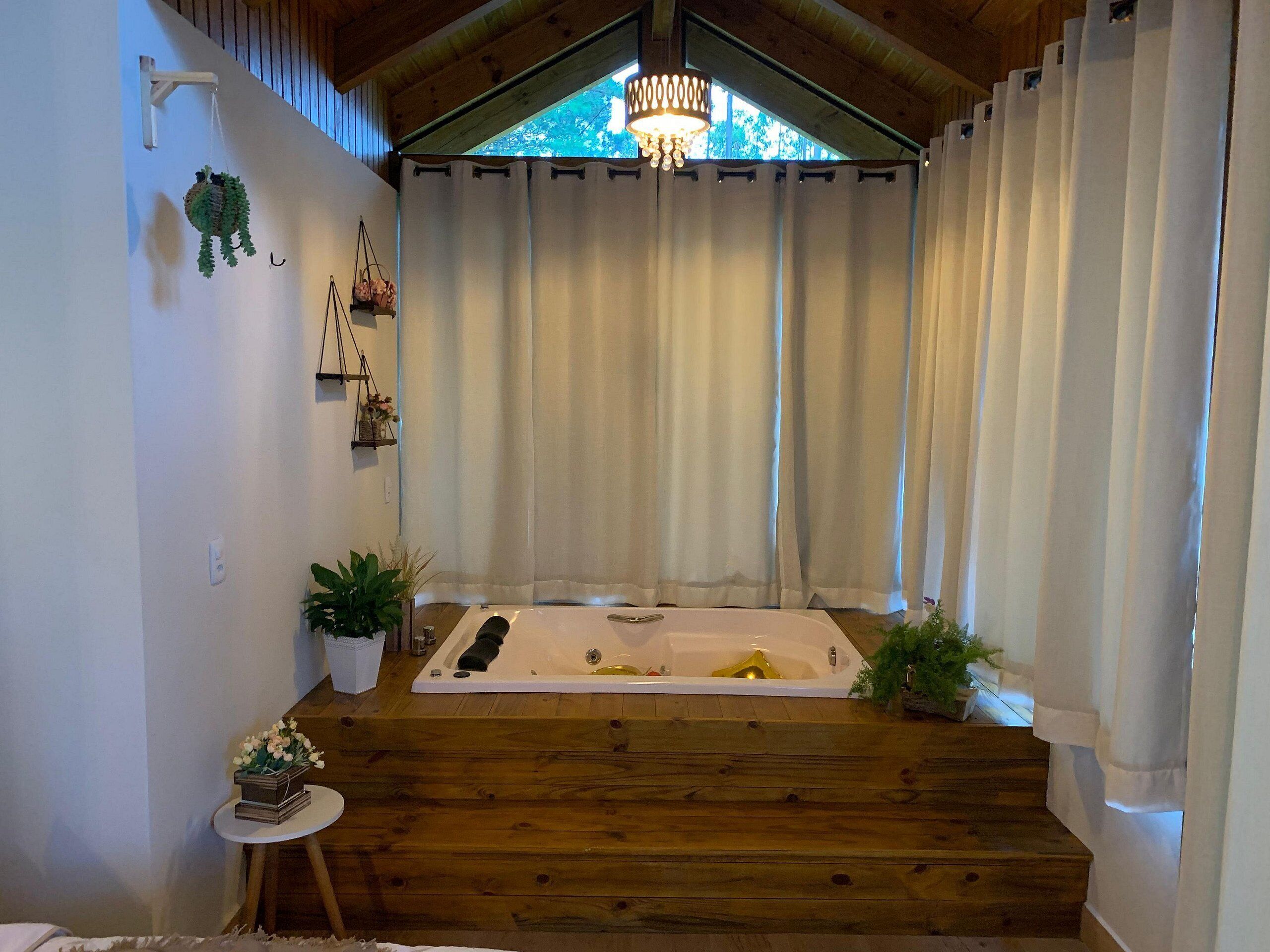 Ein Spa-Raum mit Holzboden, einer großen Badewanne und einem Fenster mit Vorhängen.