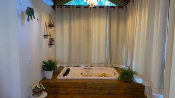 Ein Spa-Raum mit Holzboden, einer großen Badewanne und einem Fenster mit Vorhängen.
