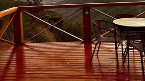Une terrasse en bois avec une table et des chaises, offrant une vue sur un paysage montagneux au coucher du soleil.