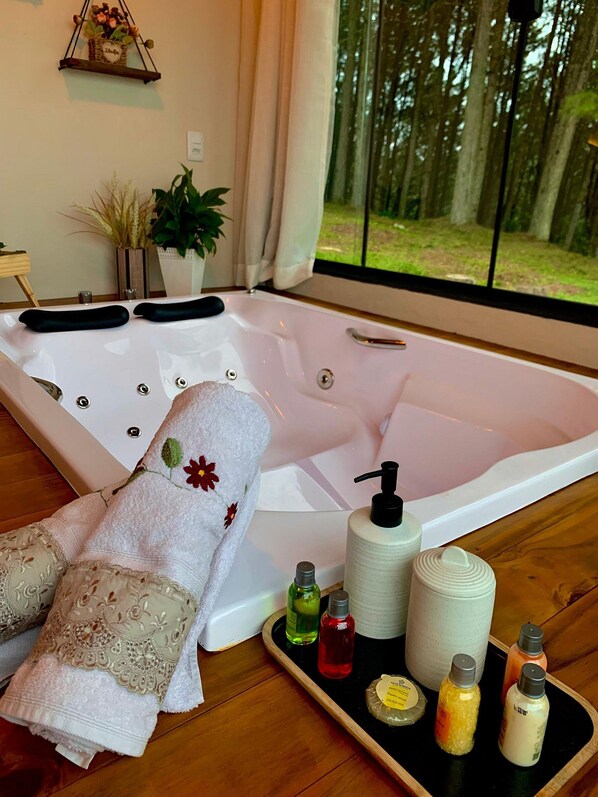A spa room with a large bathtub, towels, and toiletries. - Chalé Sossego da Montanha RanchoQueimado (Rancho Queimado)