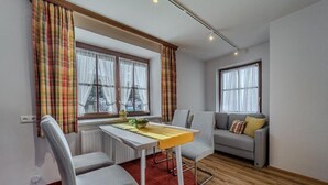 A modern living room with a dining area, featuring a sofa, chairs, a table, and large windows with curtains.