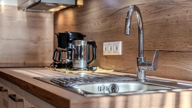 A kitchen with a stainless steel sink, a coffee maker, and a wooden countertop.
