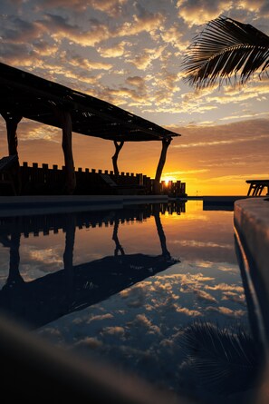 A sunset over a pool with lounge chairs and a palm tree. - Aviva, luxury de estreno en Vichayito (Vichayito)