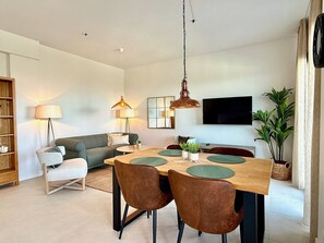 A modern living room with a dining area, a sofa, a TV, and a bookshelf.