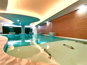 Une piscine intérieure dotée d’un espace jacuzzi, entourée de murs en bois et recouverte d’un sol carrelé.