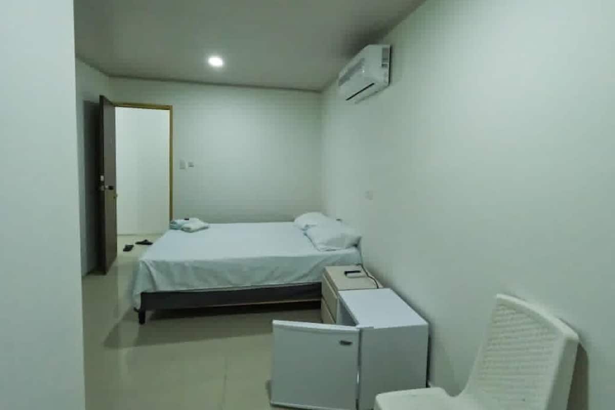 A small, clean room with a bed, a desk, and an air conditioning unit.