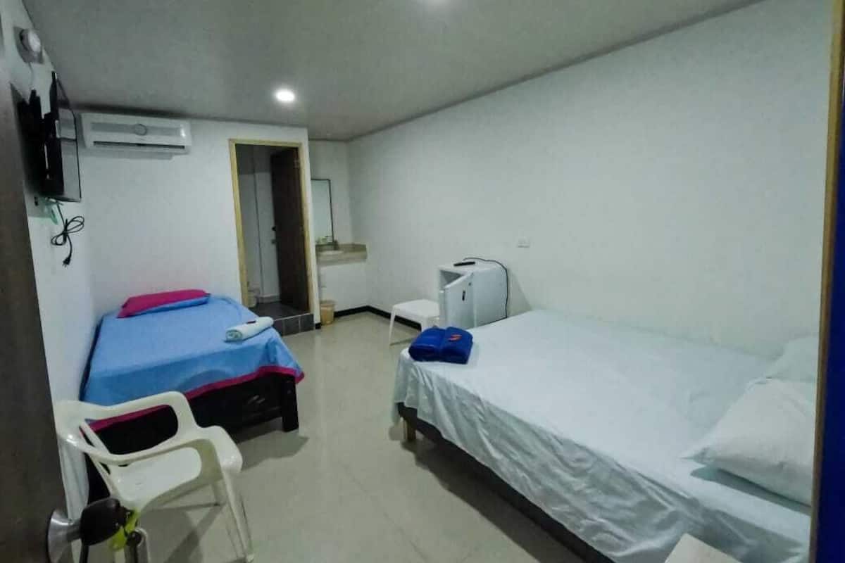 A hotel room with two beds, a desk, a chair, an air conditioner, and a TV.