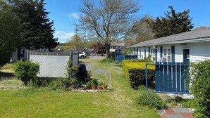 A residential area with a white house, a blue fence, and a clear sky. - Charming Studio Dennis Port Getaway with WiFi and AC - Close to Beach! (Dennis)