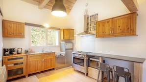 A modern kitchen with wooden cabinets, a stainless steel refrigerator, a gas stove, and a large window providing natural light.