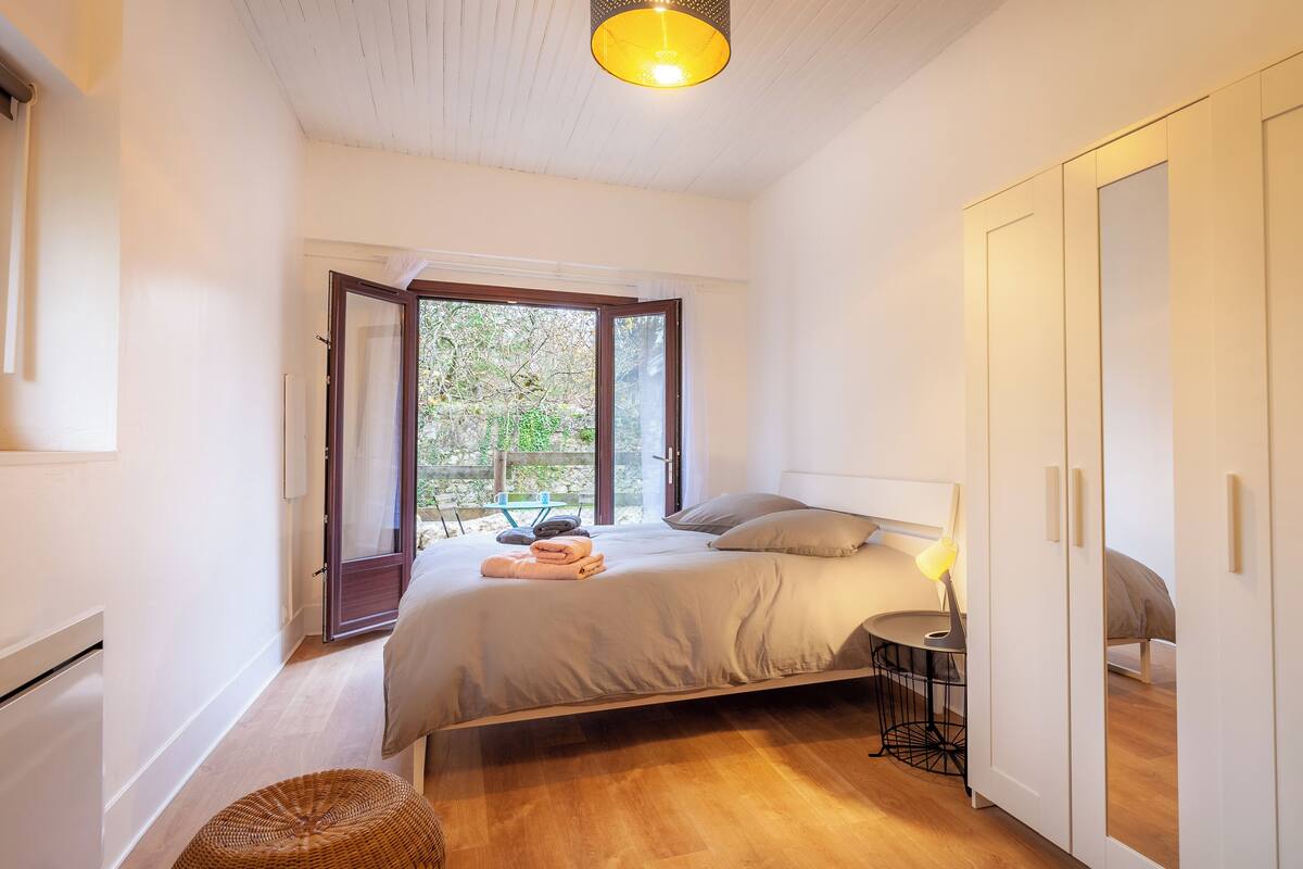 Ein Schlafzimmer mit Bett, Nachttisch und Blick ins Freie.