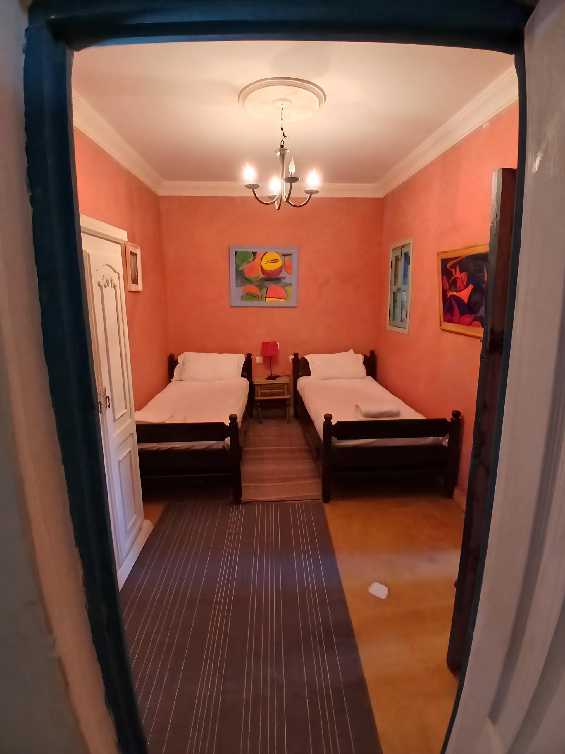 A room with two beds, a chandelier, and artwork on the walls.