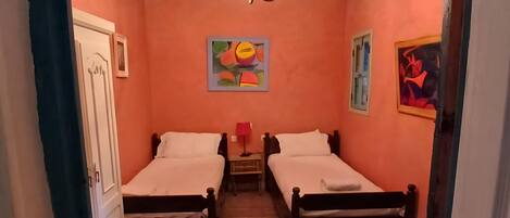 A room with two beds, a chandelier, and artwork on the walls.