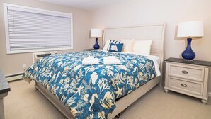 Quarto com uma cama, duas mesas de cabeceira, uma janela com persianas e um aparelho de ar condicionado fixado na parede.
