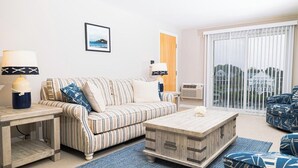 Uma sala de estar com um sofá listrado, uma mesa de centro de madeira e vista através de grandes janelas.