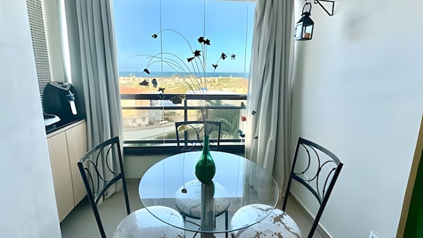 Un balcon avec une table et des chaises en verre, une vue sur la mer et une lanterne suspendue.