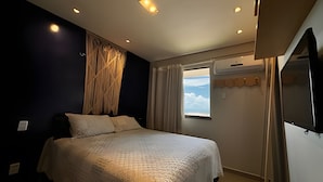 Une chambre à coucher avec un lit, une fenêtre avec des rideaux, un climatiseur et un téléviseur fixé au mur.