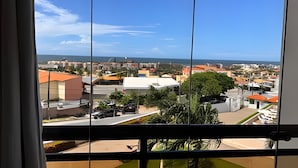 Une vue depuis une fenêtre donnant sur un paysage urbain côtier, avec des bâtiments, un ciel dégagé et une étendue d’eau à l’horizon.