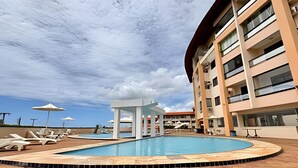 Un espace piscine doté de chaises longues et de parasols, entouré d’un immeuble à plusieurs étages avec des balcons.