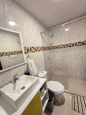Un baño moderno con salpicadero de mármol, una ducha con puerta de cristal, un inodoro y un lavabo con espejo arriba.