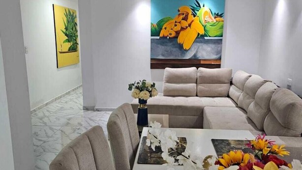 A modern living room with a sectional sofa, a dining table with chairs, and a vase of flowers. - Casa Sandunguera (Cartagena)
