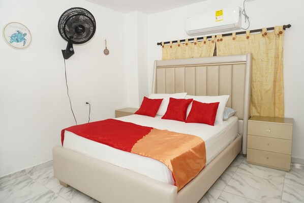 Un dormitorio con cama, mesitas de noche, ventilador de pared, aire acondicionado y cortina.