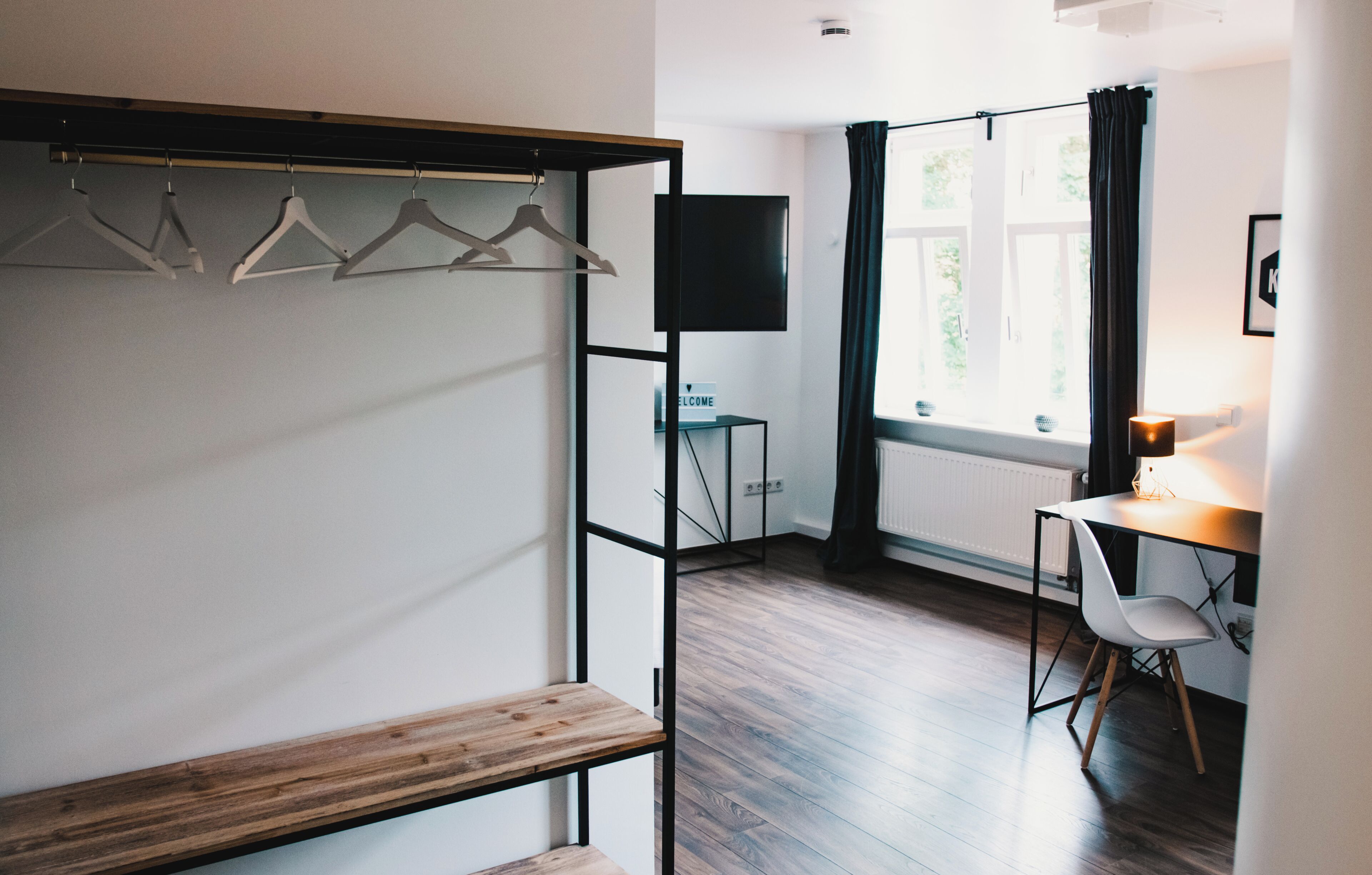 Una habitación con un banco de madera, un escritorio con una silla, un televisor y una ventana con cortinas.