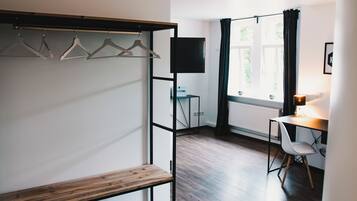 Una habitación con un banco de madera, un escritorio con una silla, un televisor y una ventana con cortinas.