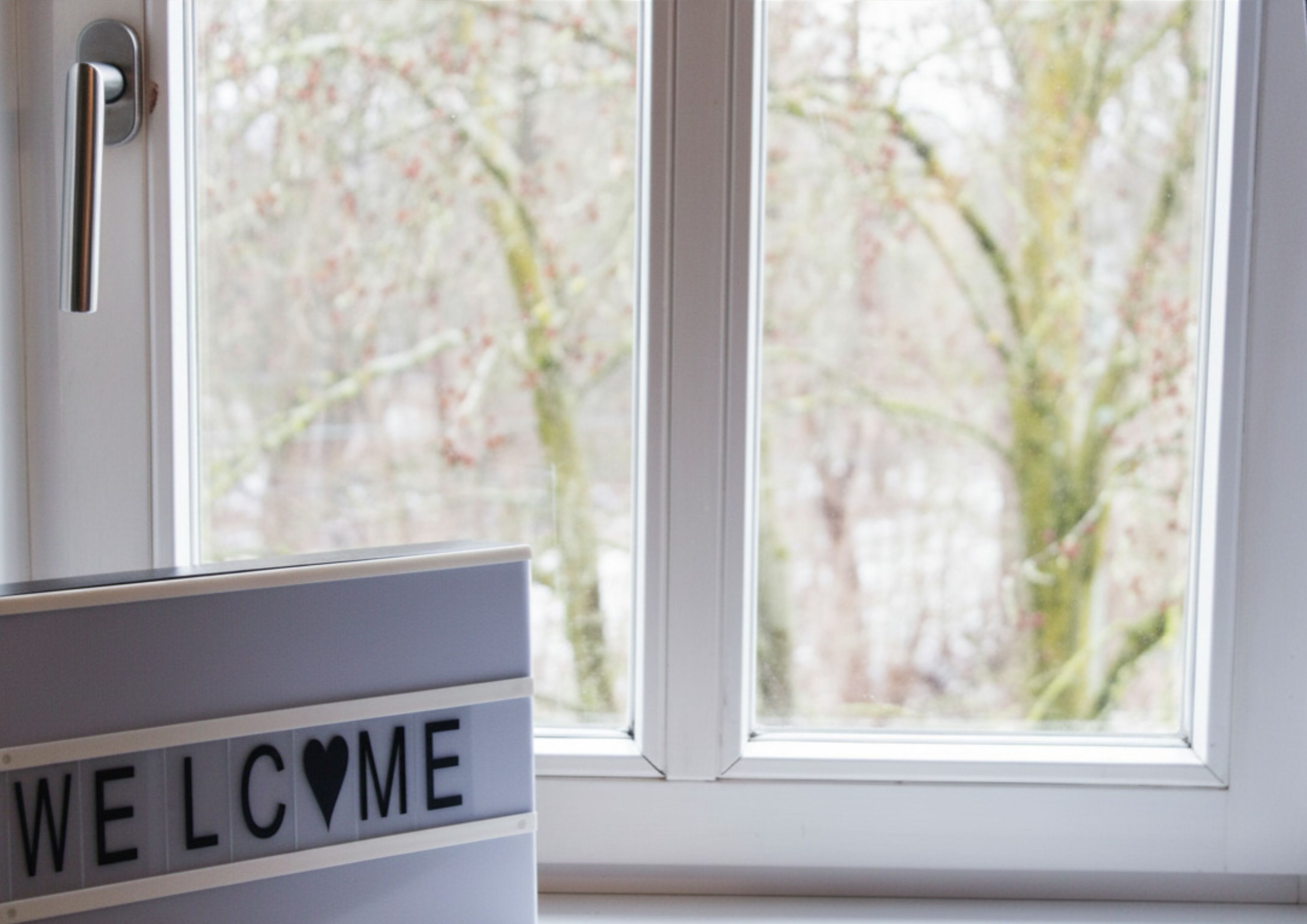 Señal que dice 'WELCOME' frente a una ventana con vistas a árboles.