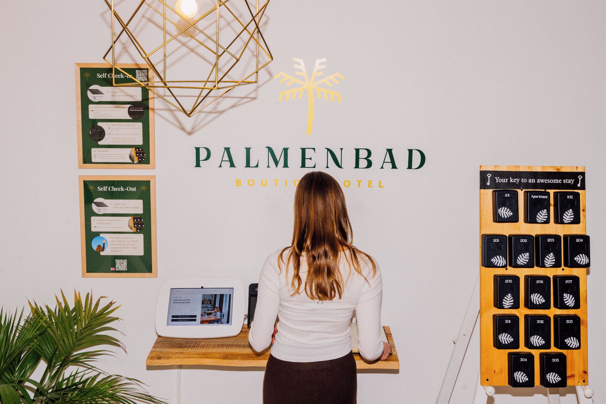Un mostrador de recepción en el Palmenda Boutique Hotel con un quiosco de auto-check-in, una exhibición de tarjetas de llave y un código QR para el auto-check-out.