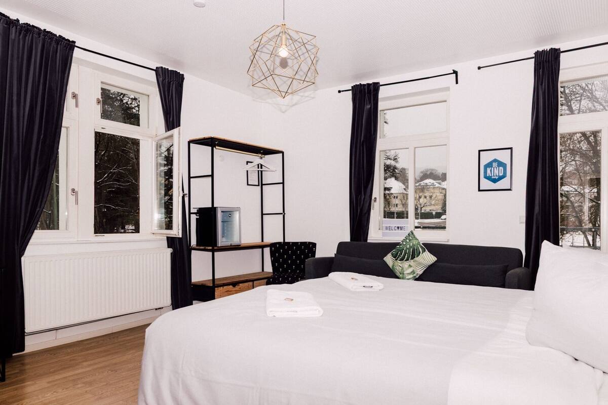 Ein Hotelzimmer mit Bett, Schreibtisch, Stuhl, einem fenster mit Vorhängen, einer Heizung und einer Wandleuchte.