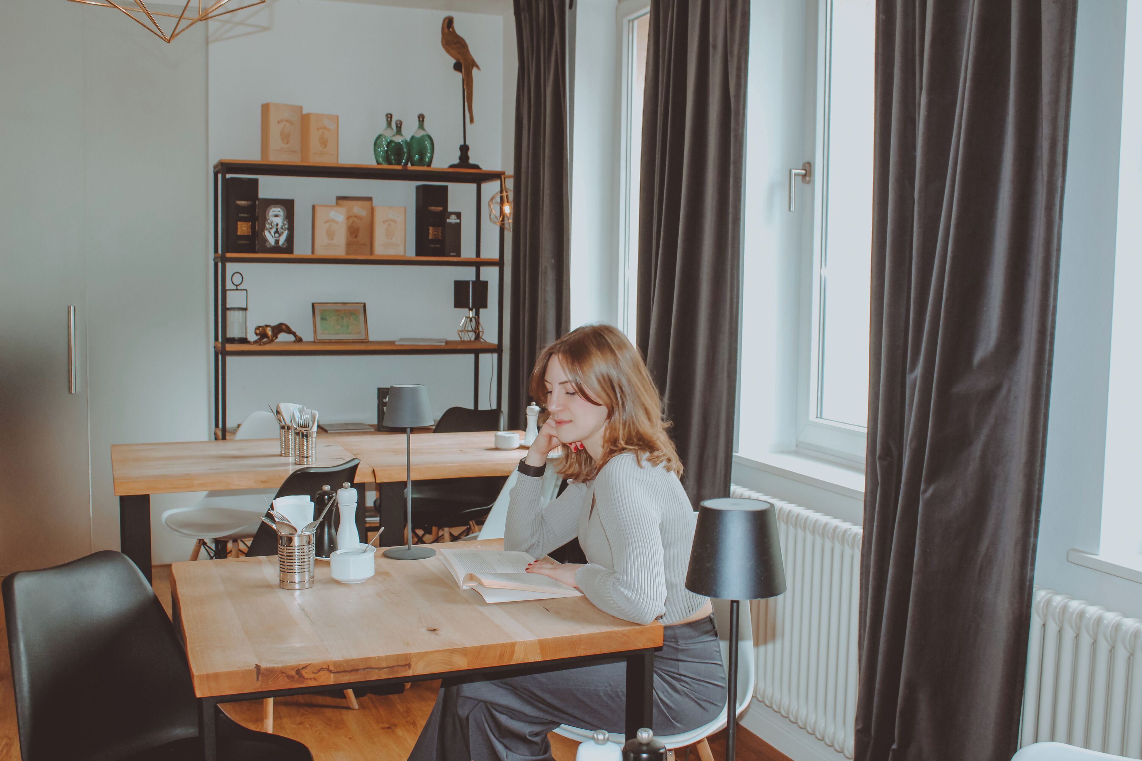 Una habitación con una mesa de comedor, sillas, una estantería y un ventanal con cortinas.