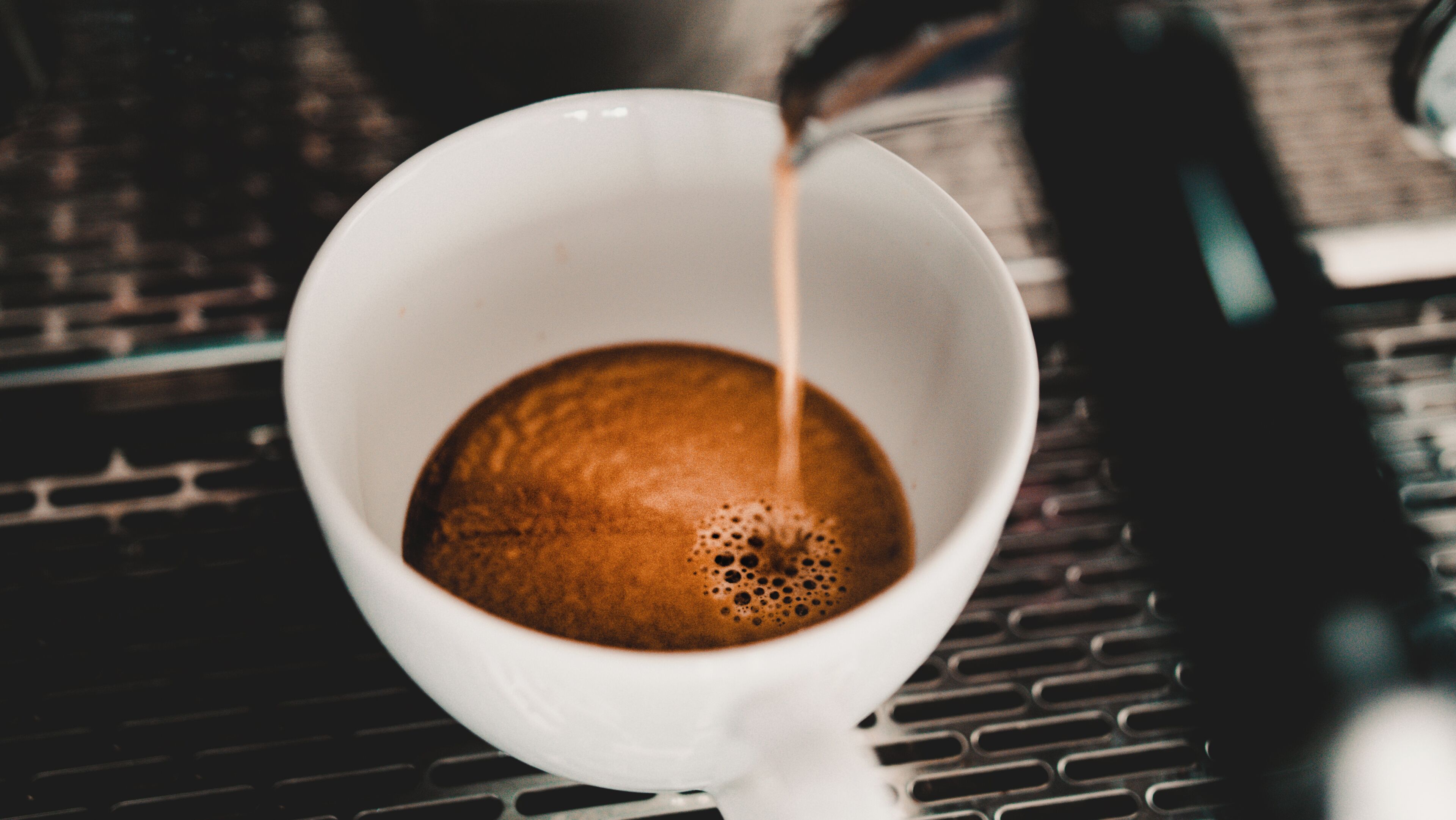 A white cup with a dark liquid, possibly coffee, being poured into it.