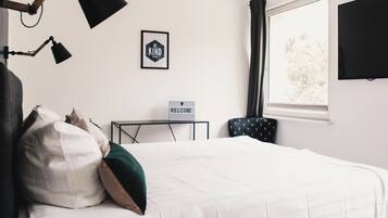 Hotelkamer met een bed, een 'WELCOME' bord, een bureau, een stoel, een televisie en een raam met gordijnen.