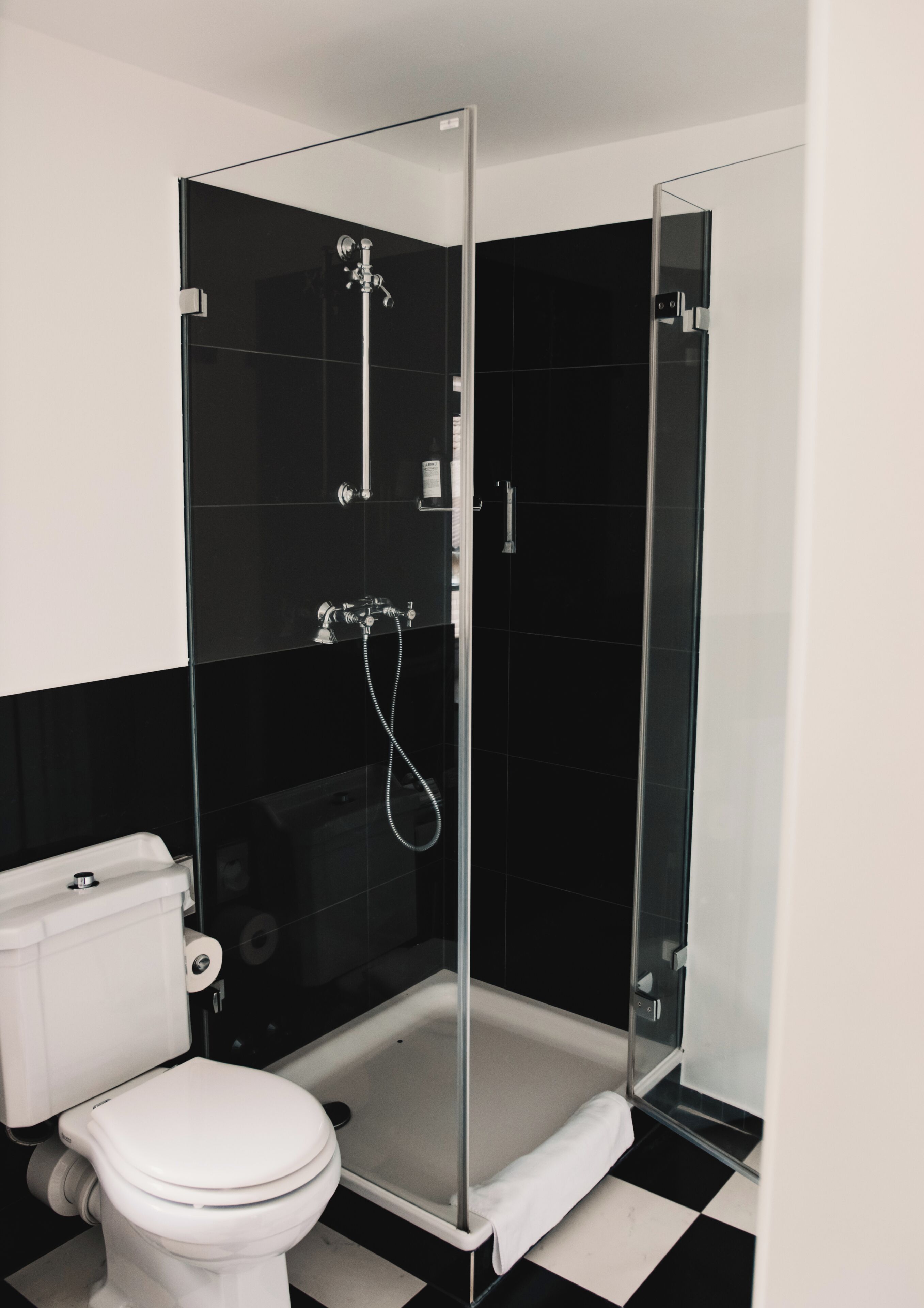 A bathroom with a glass-enclosed shower, a white toilet, and black and white checkered flooring.