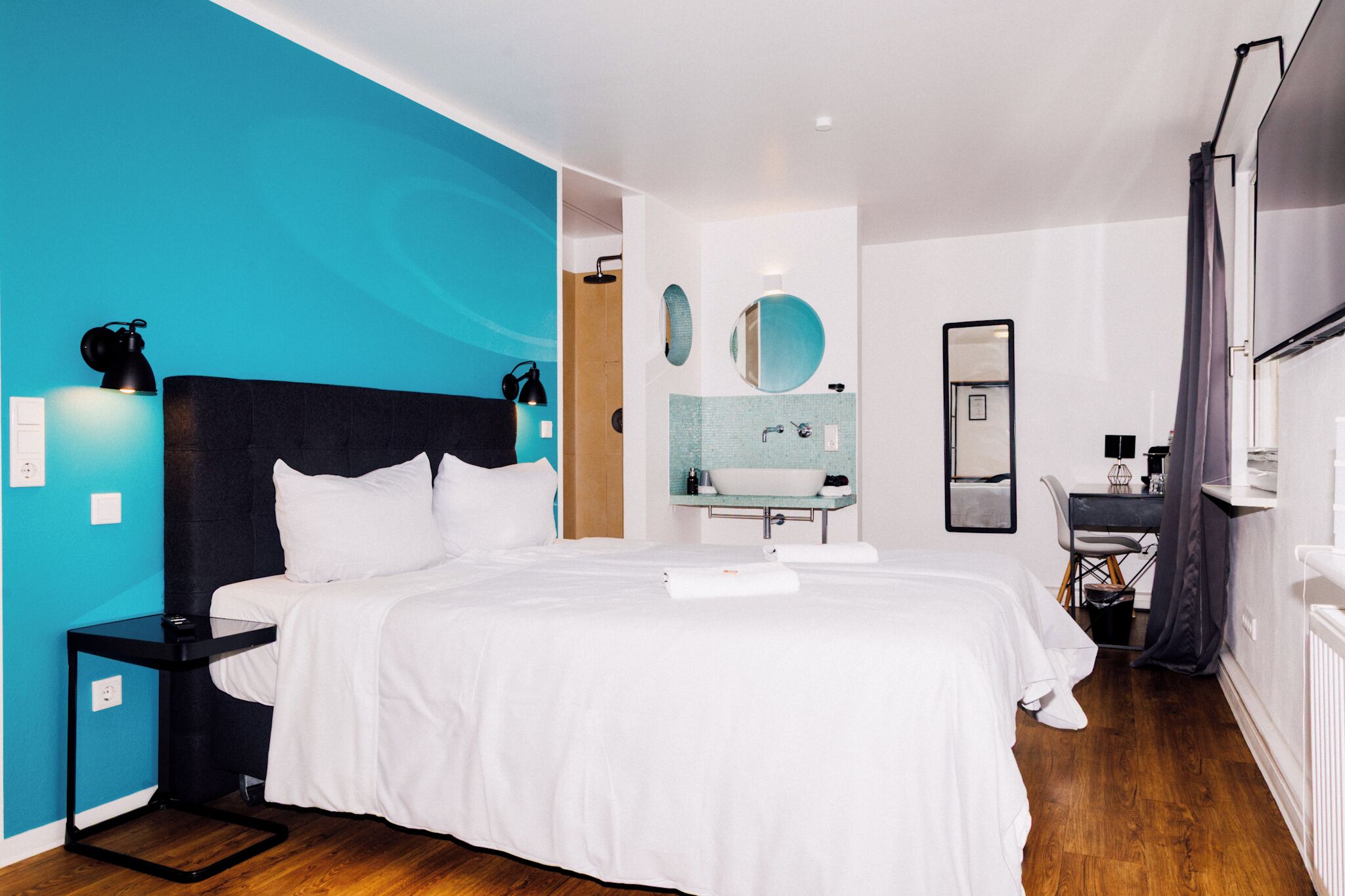 Une chambre d’hôtel moderne, dotée d’un grand lit, d’une salle de bain avec un lavabo et un miroir, et d’un bureau avec une chaise.