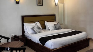 Una cama bien hecha con un cabecero de madera, dos lámparas de noche y una mesita de noche con un teléfono.