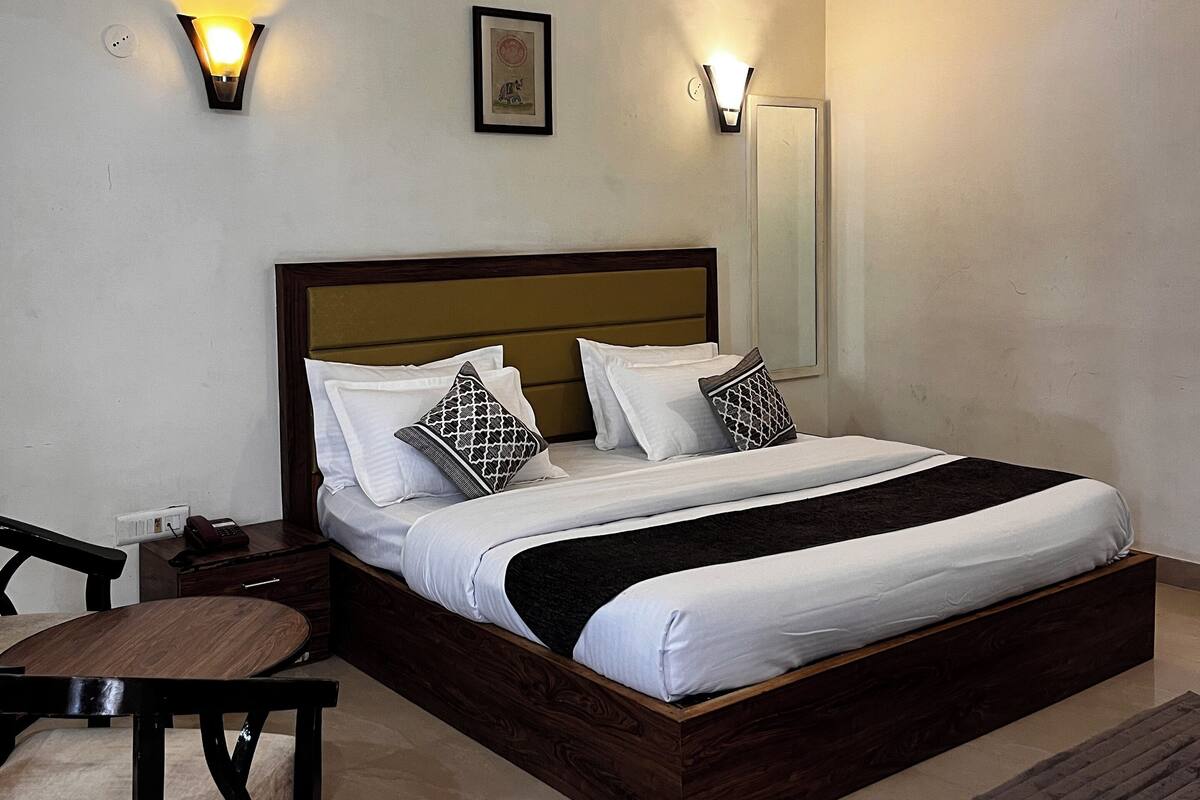 Uma cama bem arrumada com cabeceira de madeira, duas luminárias de mesa e uma mesinha de cabeceira com um telefone.