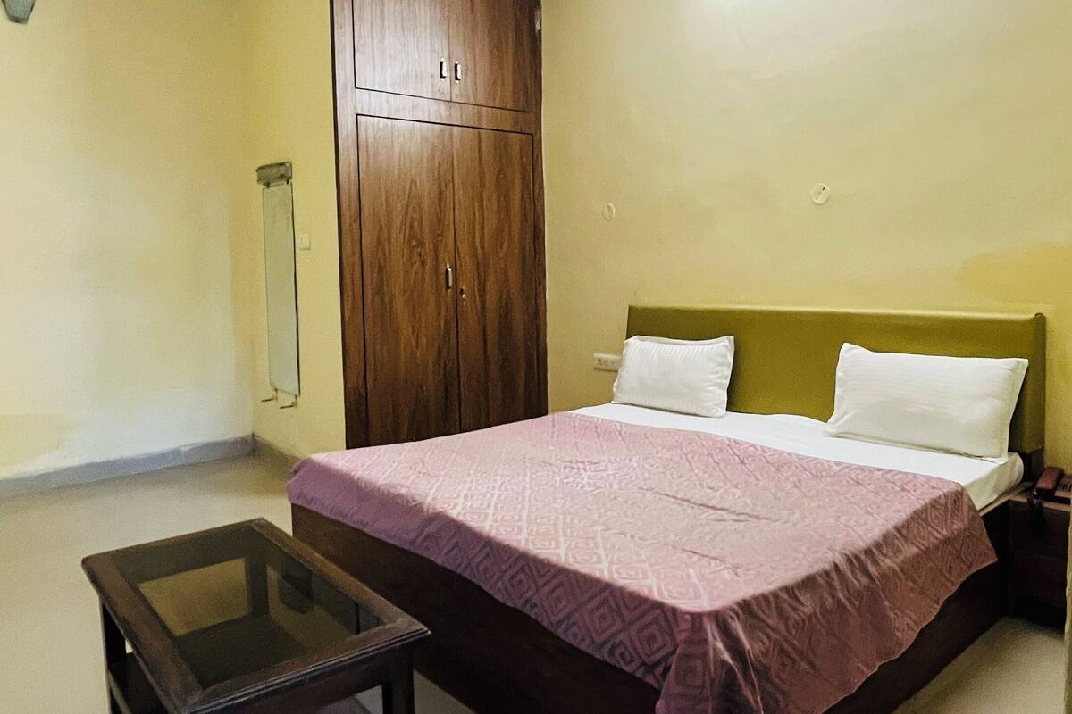Quarto com cama, mesa de cabeceira, guarda-roupa de madeira, ventilador de teto e uma pequena mesa.