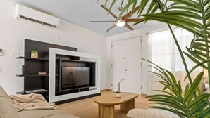 Una sala moderna con televisor de pantalla plana, ventilador de techo y una planta en maceta.