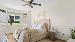 Un dormitorio con cama, ventilador de techo, mesita de noche y ventana con persianas.
