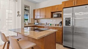 Cocina moderna con gabinetes de madera, refrigerador de acero inoxidable, microondas integrado y encimera de granito.