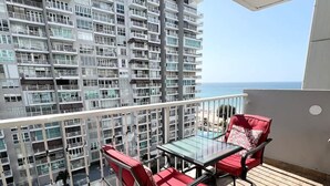 A balcony with a glass table and red chairs, overlooking a high-rise building and a clear sky. - Beachfront Paradise @ Coral Beach,  Isla Verde (Carolina)