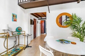 Un espace repas comprenant une table blanche, des chaises, une petite table ronde, un globe terrestre sur un socle et une plante en pot.