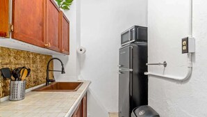 Una cocina compacta con un lavamanos, armarios de madera, un refrigerador negro y una cafetera.