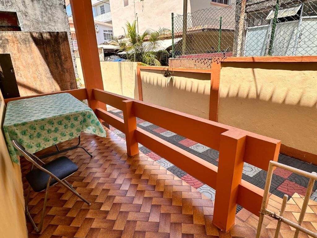 Un balcon doté d’un plancher en bois, une table recouverte d’une nappe verte et une chaise en métal.