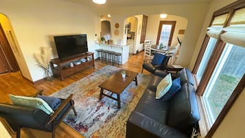 A spacious living area with a sofa, coffee table, and TV. A kitchen is visible in the background.