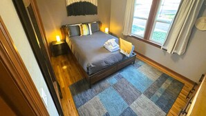 A bedroom with a bed, bedside tables, a window with curtains, and a view of the outdoors.
