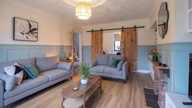 A modern living room with two grey sofas, a wooden coffee table, and a hanging light fixture. - 3br-garden-freeparking-neartowncentre (Ipswich)