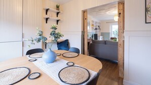 A modern dining area with a round wooden table, woven placemats, and a blue vase with green plants. - 3br-garden-freeparking-neartowncentre (Ipswich)
